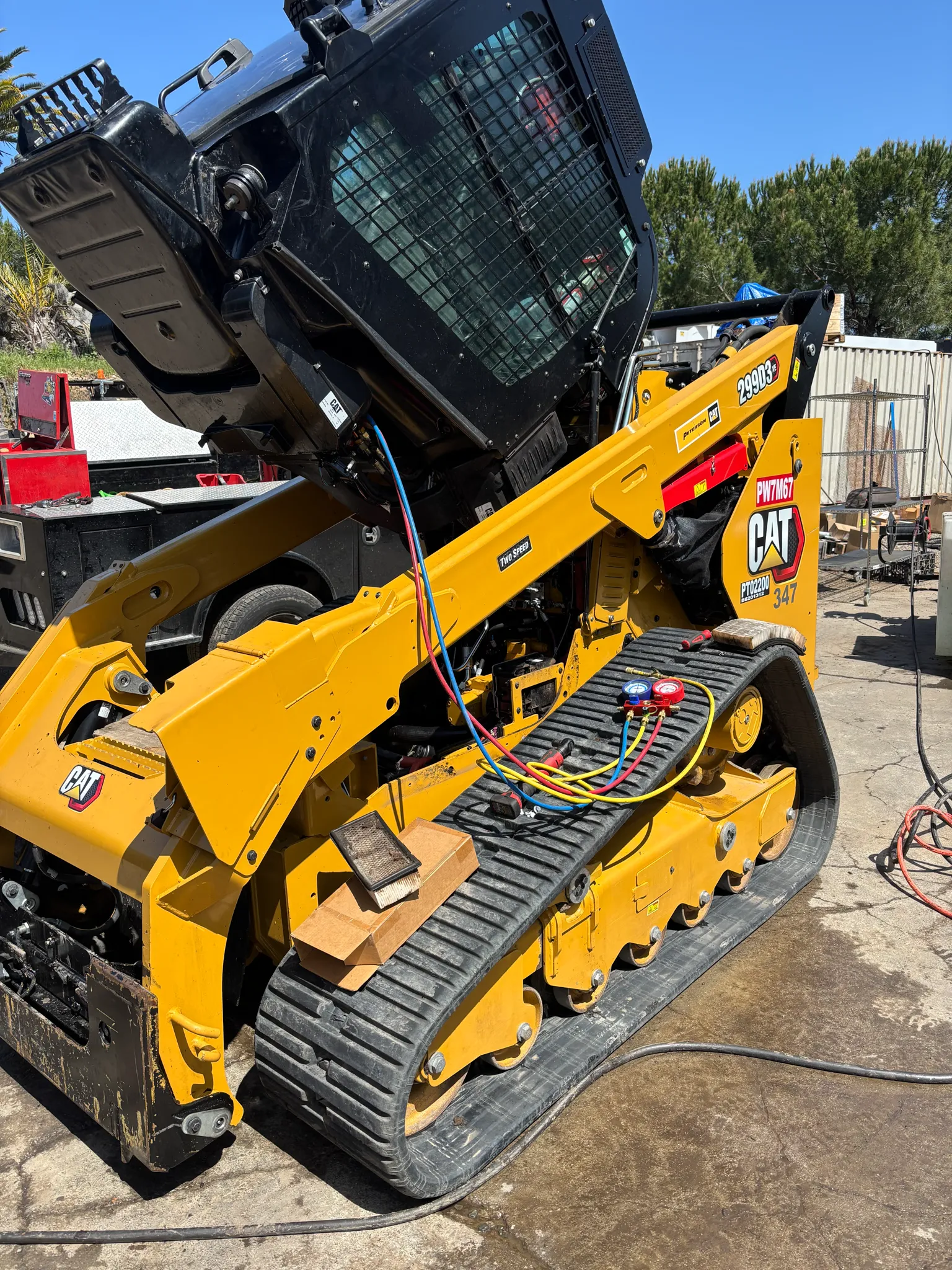 A Cat 299D3 track loader with its cab tilted up and A/C gauges hooked to the machine