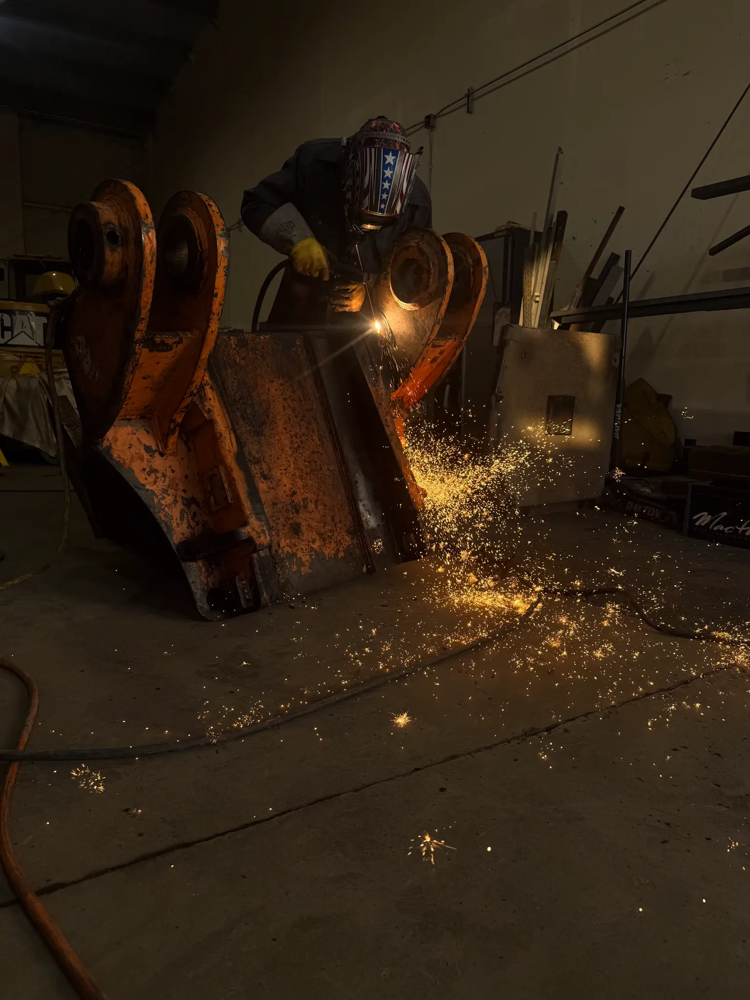 A technician welds a repair on a large excavator bucket in the shop as sparks fall to the floor