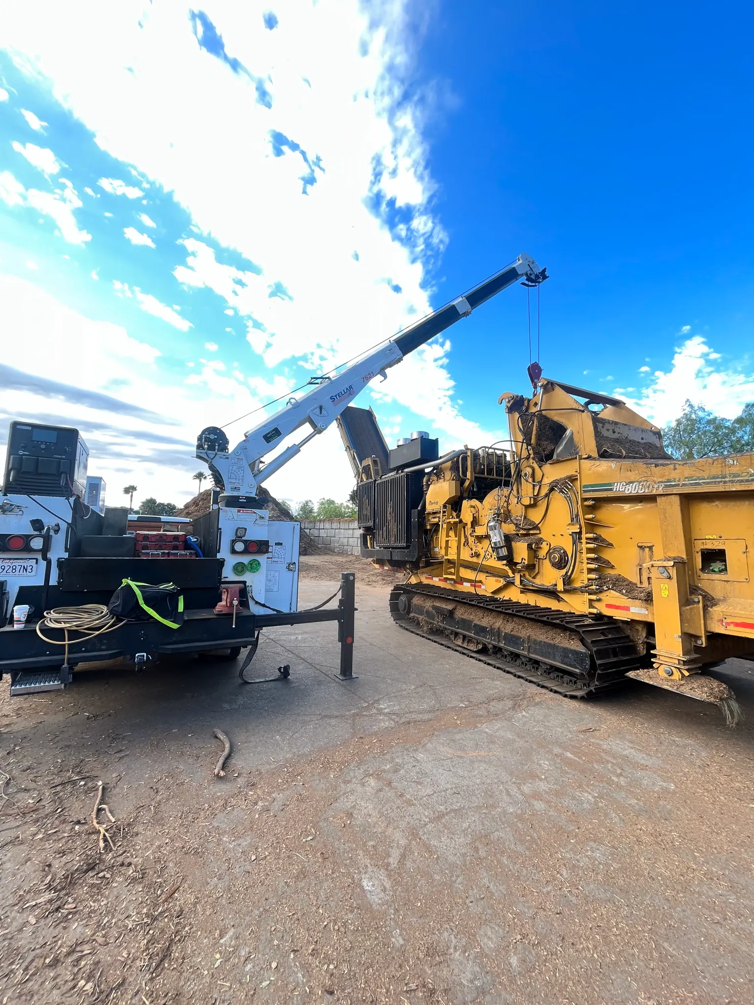A service truck with a Stellar crane parked beside a yellow tracked grinder marked HG8000TX