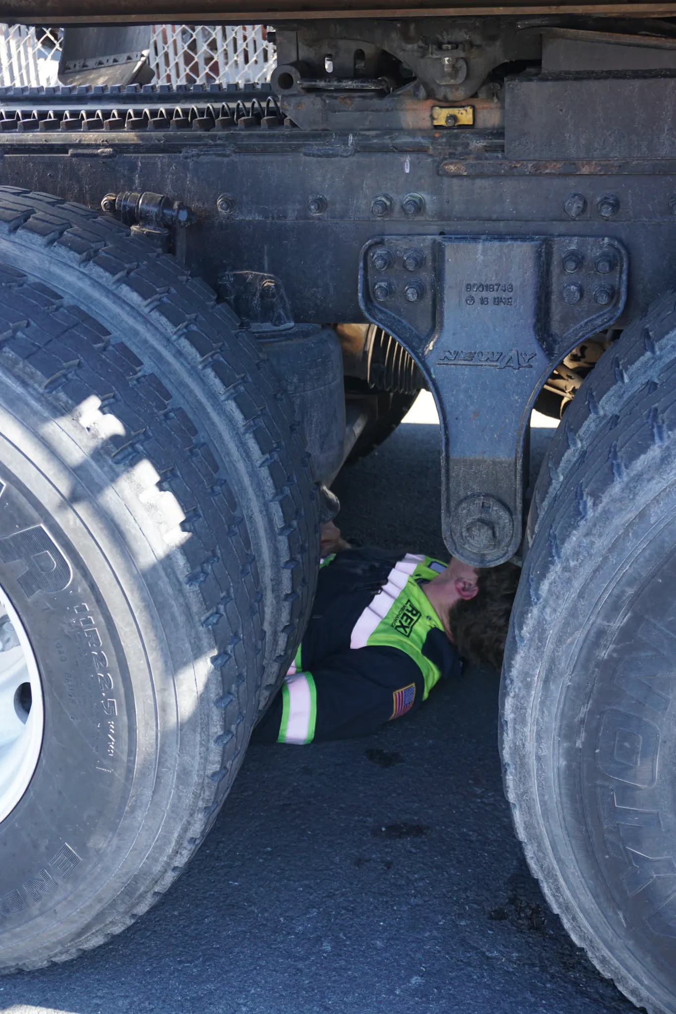 A REX Mechanical technician lies between a truck's dual tires to inspect the air suspension